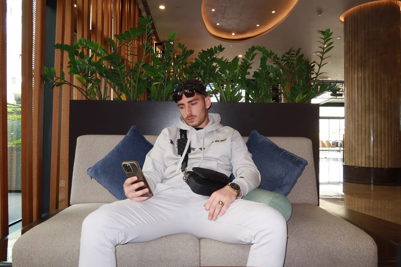 Bibz assis dans le hall d’un hôtel, téléphone à la main